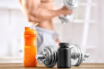 Dumbbell, jar and bottle with protein shake on table