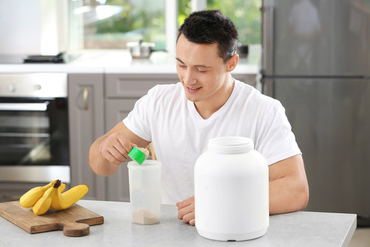Young sporty man preparing protein shake at table