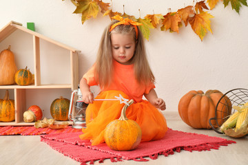 Adorable little girl with magic wand and pumpkin indoors