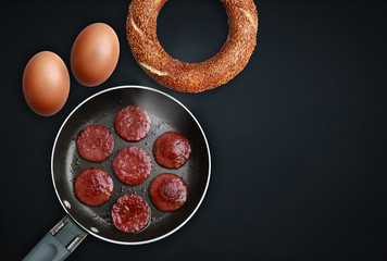 Organic brown egg, turkish bagel and sausage on a black background.
