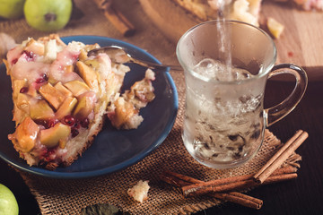 Homemade Apple pie on a round wooden board with green apples, cinnamon and red currants. Food concept. Low key image. An intimate, homely atmosphere. A beam of light on the cake and apples