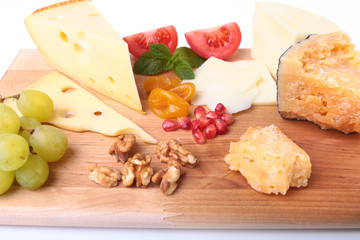 Assortment of cheese with fruits, grapes, nuts and cheese knife on a wooden serving tray.