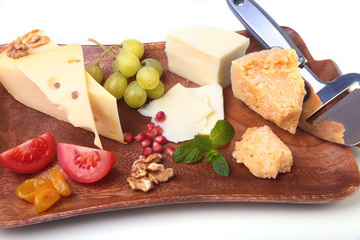 Assortment of cheese with fruits, grapes, nuts and cheese knife on a wooden serving tray.