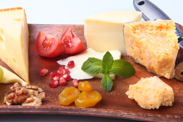 Assortment of cheese with fruits, grapes, nuts and cheese knife on a wooden serving tray.