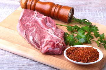 Raw beef steak with spices Leaves of coriander on wooden cutting board. Ready for cooking.