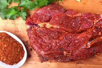Raw beef steak with spices Leaves of coriander on wooden cutting board. Ready for cooking.