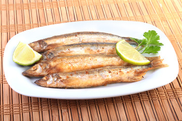 Deep frying small fish capelin and sliced lemon on white plate. Good snack to beer.