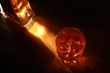 Bottle and Glass of whiskey or bourbon with ice on black stone table.