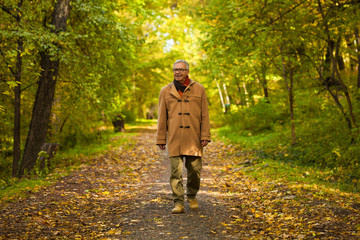 Happy senior man walking in park in autumn. 