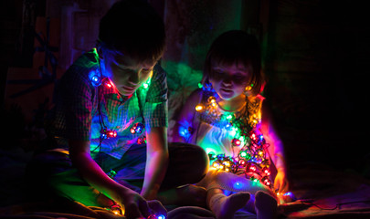 Boy and girl sitting on the floor and playing with Christmas light