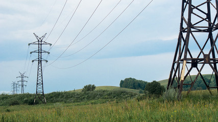 Power line towers, rusted metal beams, summer vegetation and dramatic stormy sky, clouds in...