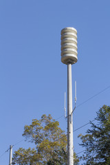 Siren tower over tree tops against a clear blue sky, space for text, vertical aspect