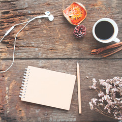 Craft notebook, pencil, cup of coffee and earphones on antique wooden table, view from above