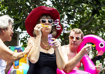 Group of diverse senior adults sitting at poolside blowing soap bubbles