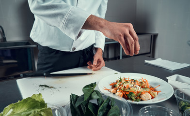 The chef prepares the dish. Sprinkle the salad with spices. Cooking. Professional kitchen. Salad dressing. Spices for salad
