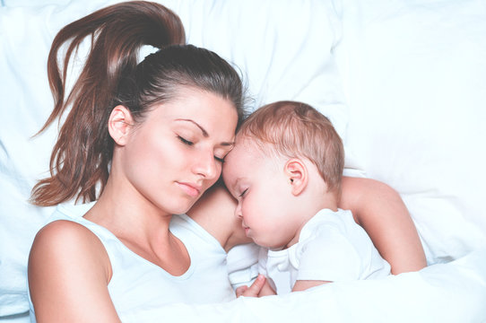 young beautiful mother hugs with her sleeping little cute son on white linen
