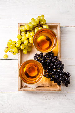 Photo on top of wooden box with two glasses of wine, black and green grapes