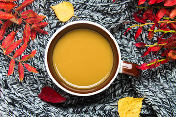 Mug of hot coffee in autumn setting on a wooden table with a knitted scarf, sweater. Comfort, warmth, cozy.