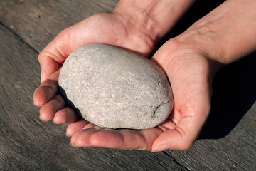 Eine Frau hält in beiden Händen einen großen platten grauen Stein über einem Holztisch...