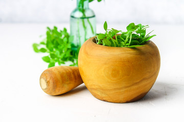 Green lemon basil in a wooden mortar on a light background. Behind the basil in the bottle.