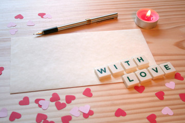 St Valentine's day: a love note for the loved one, with a pen, pink and red hearts and a candle on a wooden table
