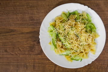 pasta farfalle salad with cucumber and cheese in plate on a wooden background. with copy space. top view