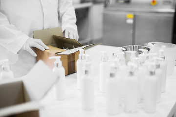 Close up of scientist hands packing cosmetics products from a lab table.