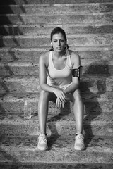 Sporty young woman sitting on stairs for resting after outdoor urban running and fitness workout.