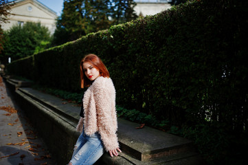 Red haired girl posed at sunny street of city.