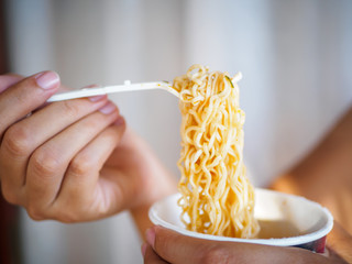 Hand holding fork to eat spicy instant noodles in cup, Sodium diet high risk kidney failure....