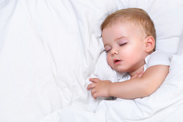 Cute one year old baby boy sleeping in a white bed
