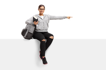 Cheerful teenage student sitting on a panel and pointing