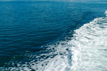 A Blue Trail Waves Surface Foam of Cruise Line After Speed Boat Passing in Ocean with Beautiful Blue Sky Background.