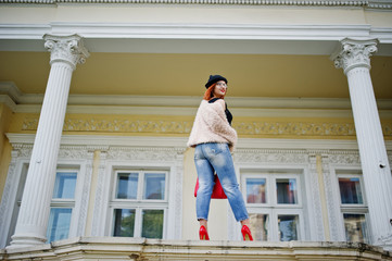 Red haired girl in glasses and hat with red handbag posed near vintage house.