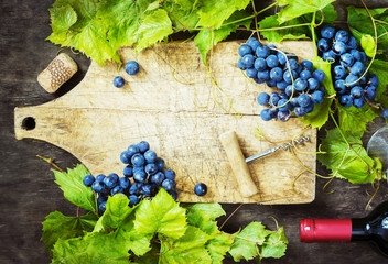 Grapes,a bottle of wine, corks and corkscrew on a wooden old table, rustic style