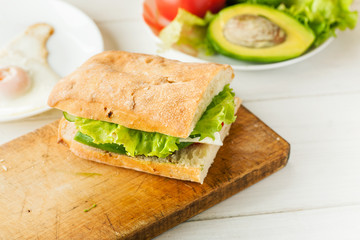 Vegetarian sandwich with avocado, tomato, egg and green salad on a wooden board