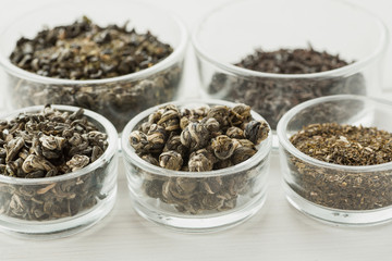 Different dry tea in a small glass dishes on a white wooden table