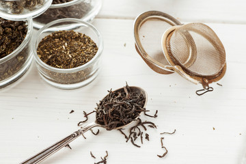 Metal strainer for tea with dry tea and metal spoon on a white wooden table