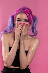 Young woman heavily madeup laughing and covering her mouth by arms.