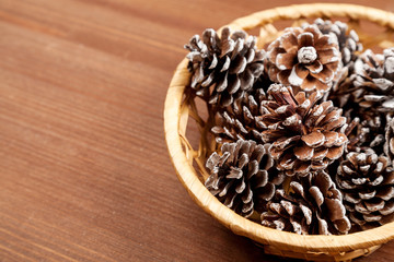 Dry fir tree cones in a wicker basket on a wooden table