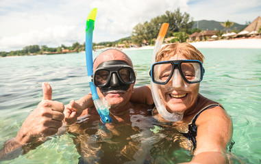 Naklejka premium Senior happy couple taking selfie in tropical sea excursion with water camera - Boat trip snorkeling in exotic scenarios - Active retired elderly and fun concept around the world - Warm bright filter