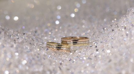 Matching wedding gold bands in three colors positioned on a flashy background made out of crystal beads
