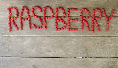 Raspberry word of fresh berries on wooden background with copy space