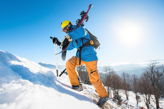 Male skier walking up the snowy hill in the mountains carrying his equipment copyspace active lifestyle sportsman seasonal recreation resort activity. Blue sky and winter forest on the background