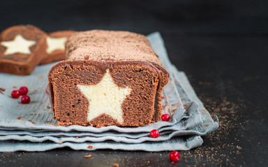 A very chocolate cake covered with dark chocolate and sprinkled with cocoa with a vanilla star inside. On a wooden dark background. Decorated with fresh cranberries, The perfect cool Christmas dessert