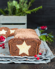 Fototapeta na wymiar A very chocolate cake covered with dark chocolate and sprinkled with cocoa with a vanilla star inside. On a wooden dark background. Decorated with fresh cranberries, The perfect cool Christmas dessert