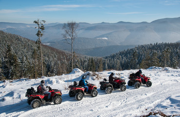 Four ATV riders on off-road quad bikes on snow at top of the mountain in winter