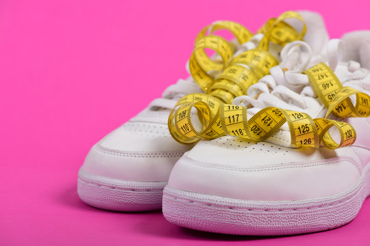 Sneakers with measuring tape on pink background.