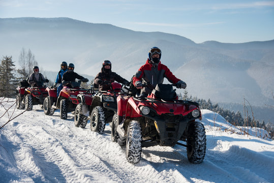Four ATV riders on off-road four-wheelers ATV bikes on snow in the winter mountains