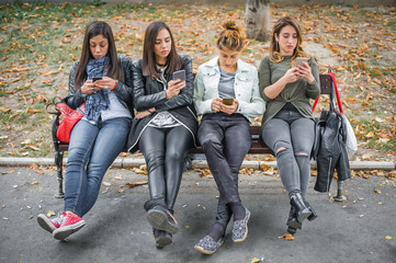 Obraz na płótnie Canvas Group of girls using cellphones on park bench